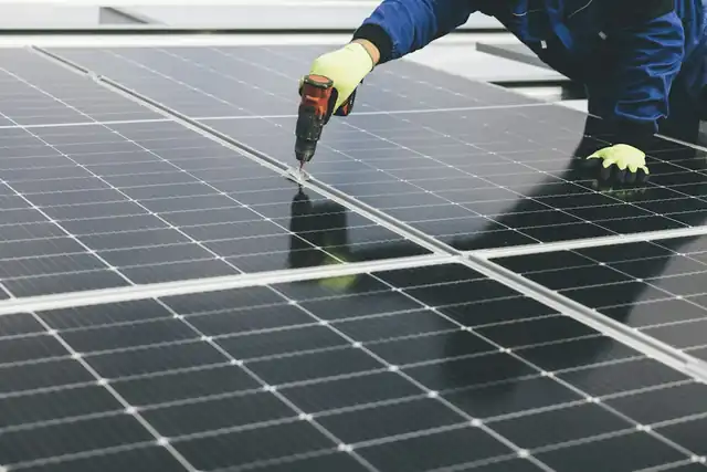 An engineer in gloves working on a row of solar panels